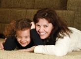 Smiling mom and daughter laying on clean carpet