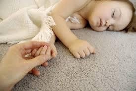 Child sleeping on clean gray carpet holding someone's hand