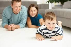 Mom and dad laying on clean white carpet, watching child crawl