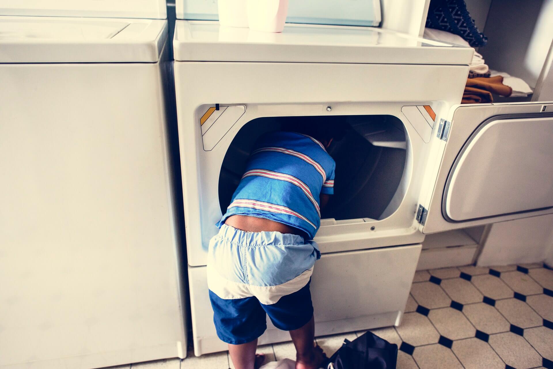 young boy sticking head inside dryer